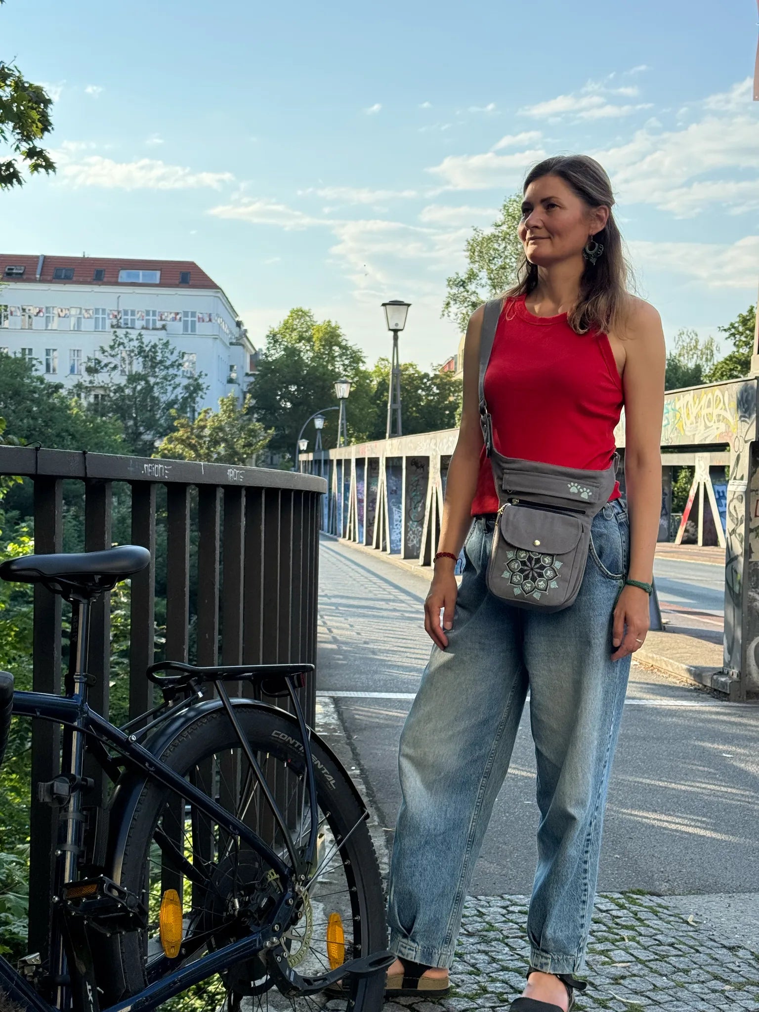 Frau trägt eine graue NIJENS Super-Hannover Gassi-Tasche mit Mandala-Stickerei als Crossbody beim Spaziergang in der Stadt.
