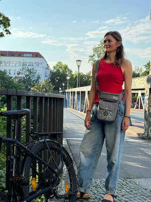 Frau trägt eine graue NIJENS Super-Hannover Gassi-Tasche mit Mandala-Stickerei als Crossbody beim Spaziergang in der Stadt.