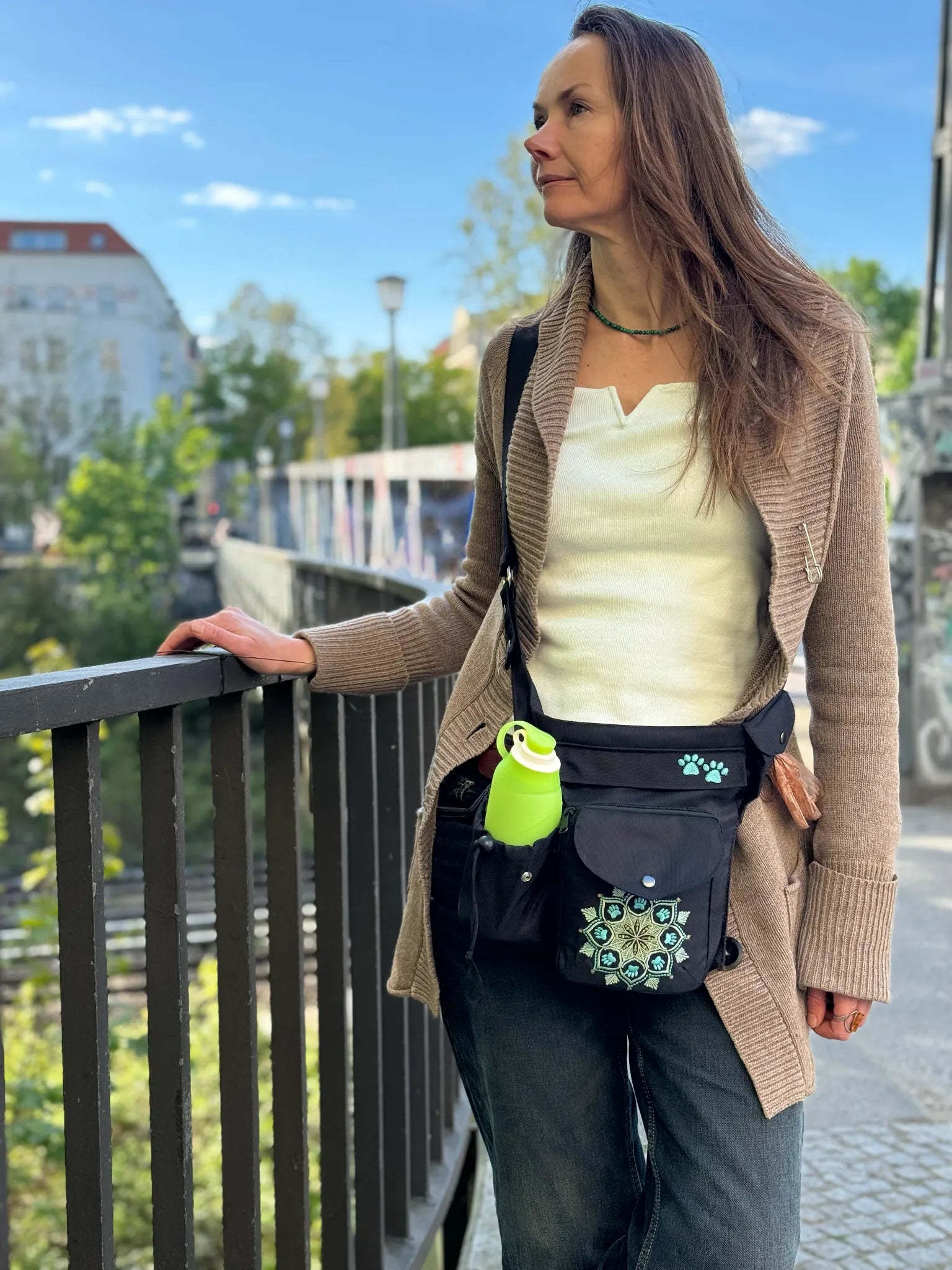 Frau trägt die wasserabweisende Nijens Gassitasche Brandenburg mit Mandala-Stickerei und Flaschenhalter als Crossbody auf einem Spaziergang in der Stadt.