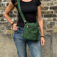 Frau mit schwarzem Oberteil und Jeans trägt eine grüne Crossbody Gassi-Tasche mit Flaschenfach