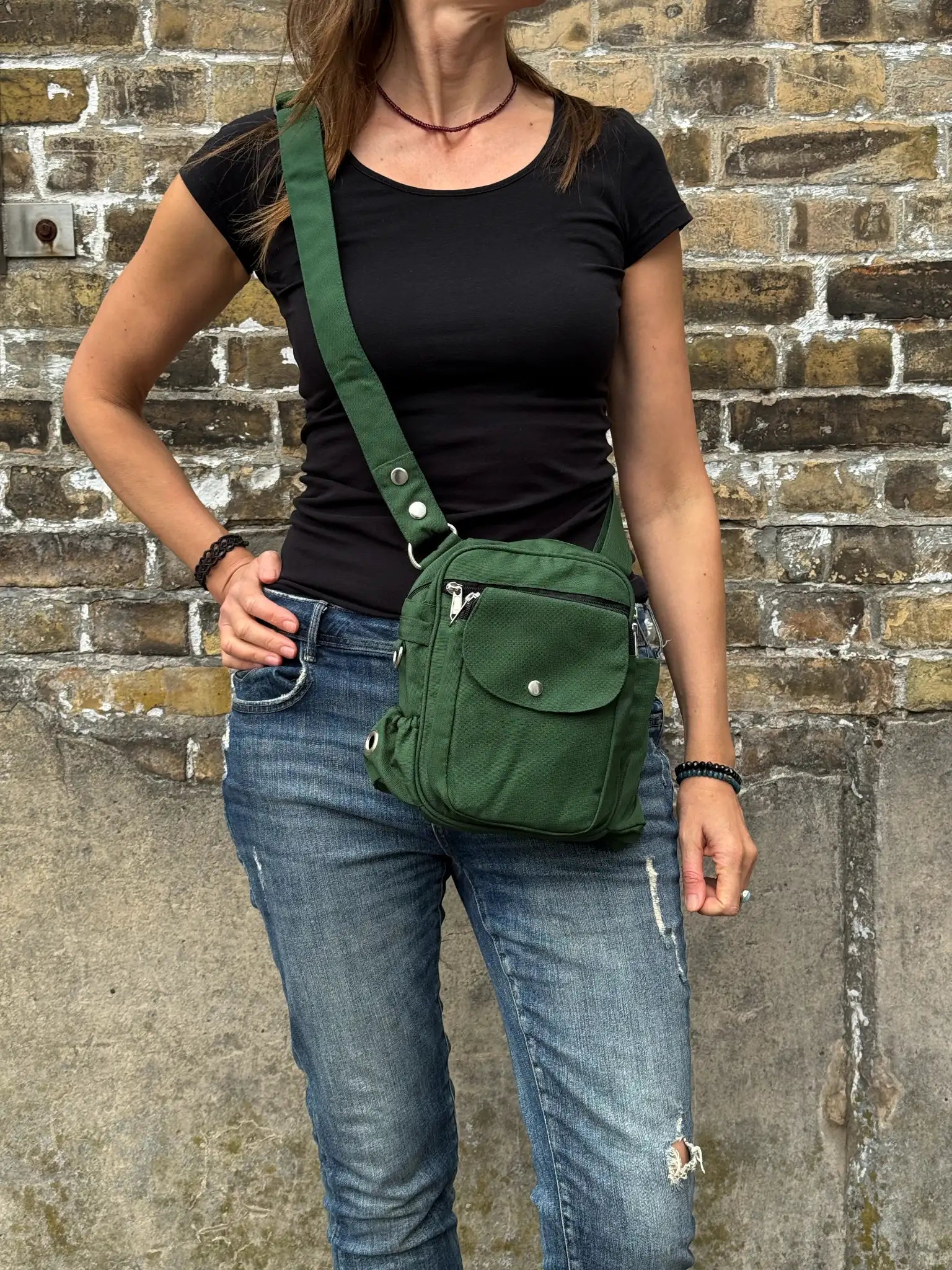 Frau mit schwarzem Oberteil und Jeans trägt eine grüne Crossbody Gassi-Tasche mit Flaschenfach