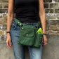 Frau mit schwarzem Oberteil und Jeans trägt eine grüne Nijens Gassi-Tasche mit Flaschenfach