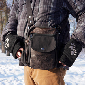 Gassi-Tasche Nijens Konstanz in Braun-Schwarz mit geprägtem Muster, getragen als Hüfttasche im Winter – dazu schwarze Handschuhe mit Pfotenmotiv, ideal für Hundespaziergänge bei kaltem Wetter