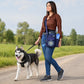 Frau mit dunkelblauer Nijens Hüfttasche und Sportschuhen spaziert mit einem Husky auf einem Feldweg in der Natur.