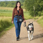 Frau mit schwarzer Nijens Hüfttasche und Sportschuhen spaziert mit einem Husky auf einem Feldweg in der Natur.