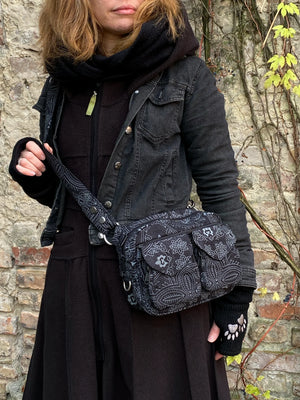 UmhĂ€ngetasche aus Canvasstoff, Schwarz mit floralen Ornamenten.