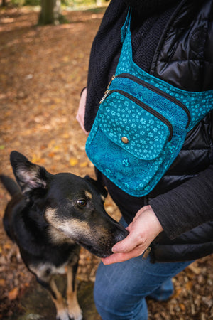 Modell präsentiert Gassitasche aus Stoff mit Pfoten-Motiv in Türkis für Hundetraining. Mit herbstlichen Blättern im Hintergrund.