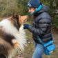 Frau im Park mit Collie-Hund trägt eine türkise Nijens Gassitasche mit Mandala-Stickerei, blaue Strickmütze und Armstulpen.