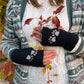 Nahaufnahme Hände von Model mit Handgestrickte Pulswärmer, Armstulpen mit Zwei-Pfoten-Stickerei aus Schurwolle in Schwarz. Innenfutter: Fleeceeinsatz. Spalt für Daumen.
