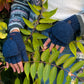Handmodell vor herbstlicher Kulisse mit fingerlose Handschuhe aus Schurwolle in Petrol mit Fleeceeinlage und einer umklappbaren Fingerabdeckung, welche mit einem Holzknopf auf dem Handrücken fixiert werden kann.