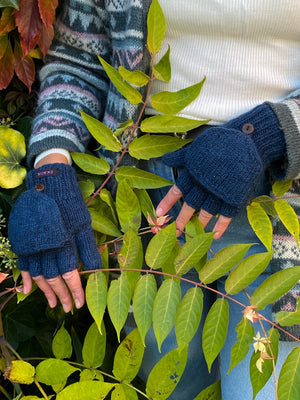 Handmodell vor herbstlicher Kulisse mit fingerlose Handschuhe aus Schurwolle in Petrol mit Fleeceeinlage und einer umklappbaren Fingerabdeckung, welche mit einem Holzknopf auf dem Handrücken fixiert werden kann.