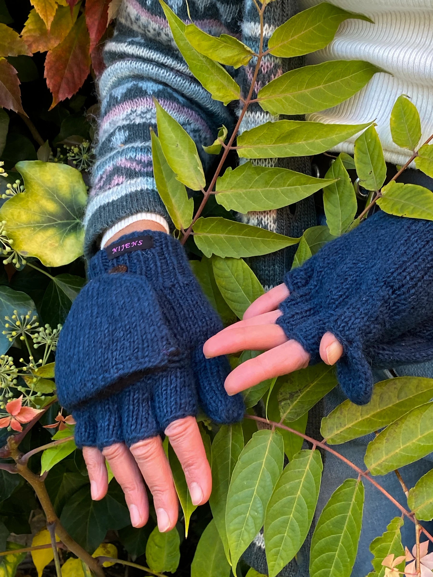 Handmodel mit fingerlose Handschuhe aus Schurwolle in Petrol mit Fleeceeinlage und einer umklappbaren Fingerabdeckung, welche mit einem Holzknopf auf dem Handrücken fixiert werden kann.