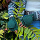 Model präsentiert fingerlose Handschuhe aus Schurwolle in Dunkelgrün mit Fleeceeinlage. Durch eine umklappbare Fingerabdeckung können die fingerlosen Handschuhe auch als Fäustlinge getragen werden.