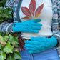 Handmodel vor herbstlicher Kulisse präsentiert handgestrickte Handschuhe aus Schurwolle in Türkis mit Fleeceinlage und Zopfstrickmuster auf dem Handrücken.