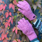 Handmodell präsentiert handgestrickte Handschuhe aus Schurwolle in Rosa mit Fleeceinlage und Strickmuster vor herbstlichen Blättern.