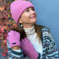 Modell vor herbstlicher Kulisse präsentiert Handgestrickte Handschuhe aus Schurwolle in Rosa mit Fleeceinlage und Zopfstrickmuster.