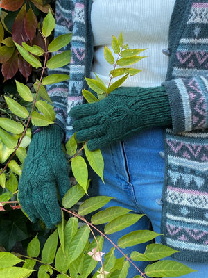 Modell vor herbstlicher Kulisse präsentiert handgestrickte Handschuhe aus Schurwolle Dunkelgrün mit Fleeceeinlage und Strickmuster.