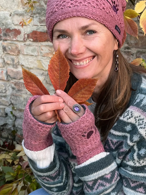 Model präsentiert handgestrickte Pulswärmer mit Zwei-Pfoten-Stickerei aus Schurwolle in Altrosa. Spalt für Daumen und eine dazu passende Wollmütze mit Herz und Pfoten Stickerei an der Seite.