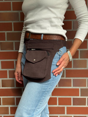 Eine Frau präsentiert eine Bauchtasche aus robustem Baumwollstoff in Schokobraun. 