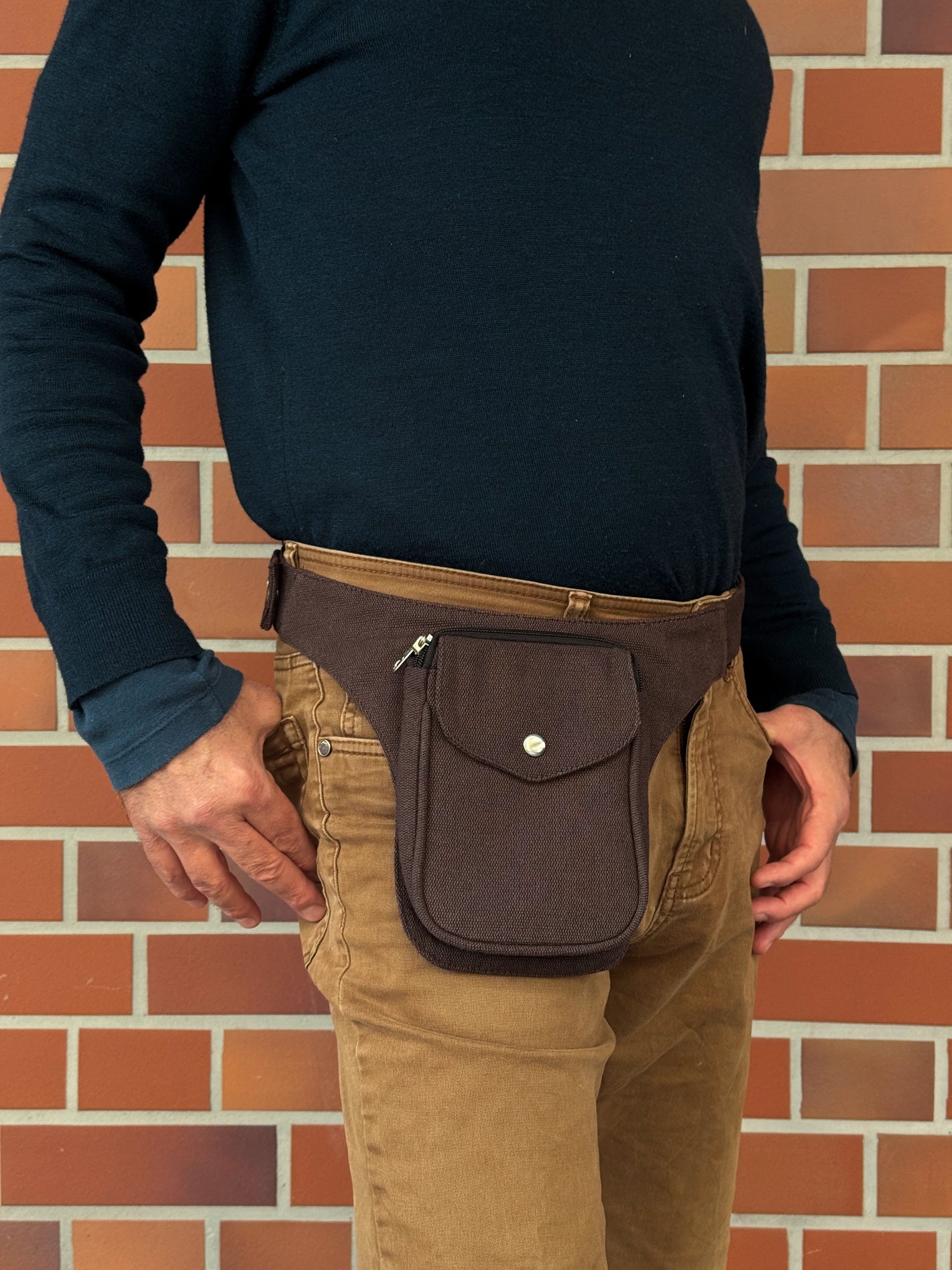 Model präsentiert kleine Bauchtasche aus robustem Baumwollstoff in Schokobraun. 
