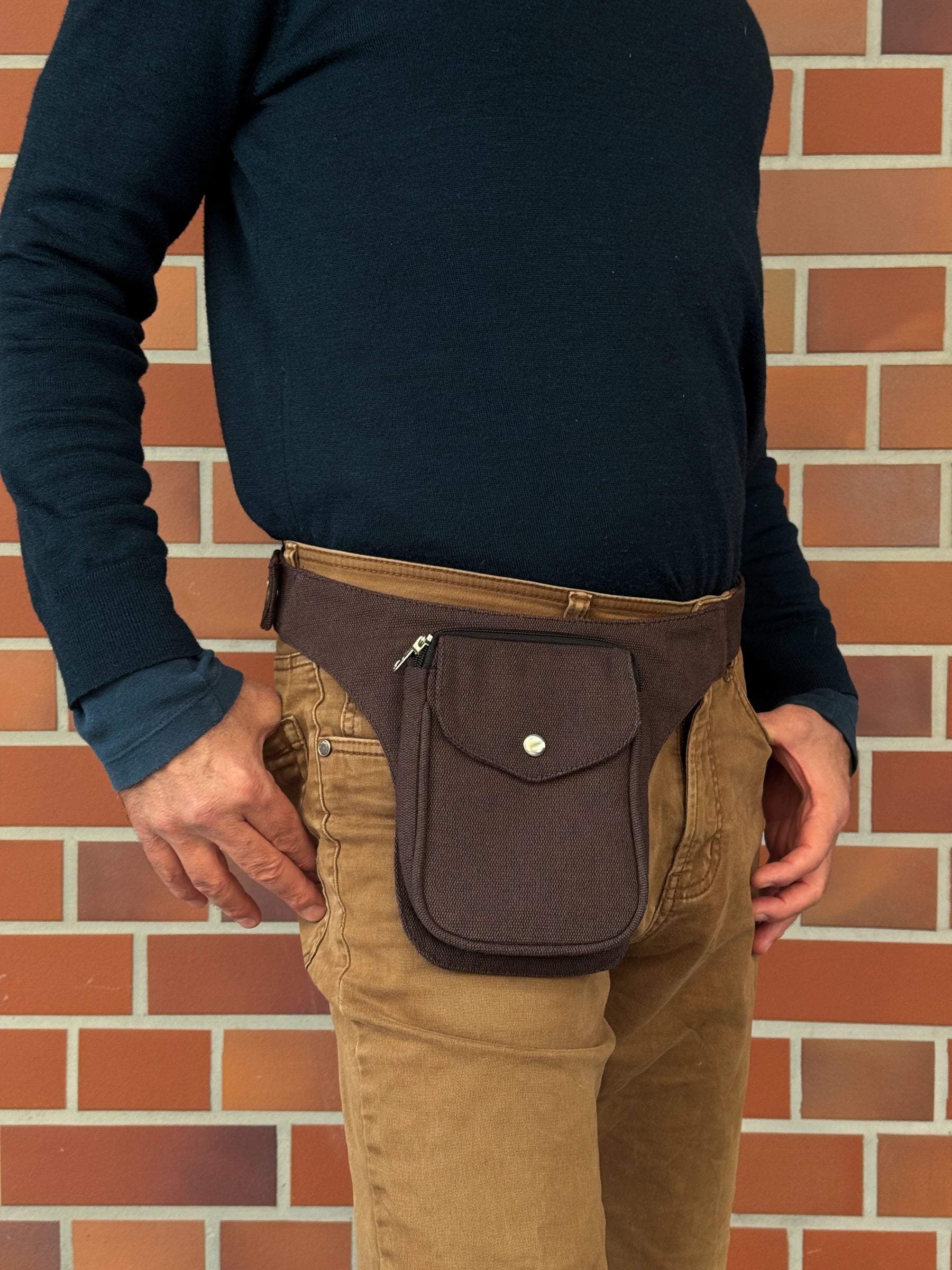 Model präsentiert kleine Bauchtasche aus robustem Baumwollstoff in Schokobraun. 