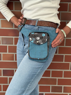 Model präsentiert kleine Bauchtasche aus robustem Baumwollstoff in grau, hellblau mit Muster und großen Pfoten-Print. 