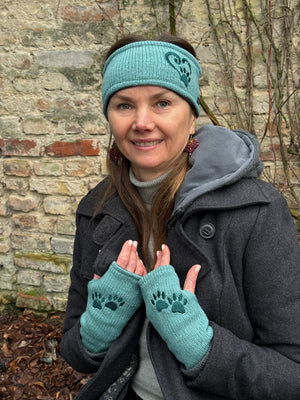 Auf dem Kopf trägt das Model Nijens Stirnband SIMPLONE HP 51 aus Schurwolle in Türkis mit Herz & Pfotestickerei. An den Händen die passenden Handstulpen HADAR 48 aus Schurwolle in Türkis mit zwei Pfotenstickerei.