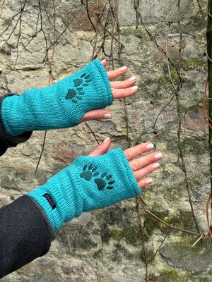 Nahaufnahme Hände: Ein Model präsentiert die Handstulpen HADAR 48 aus Schurwolle in Türkis mit zwei Pfotenstickerei.