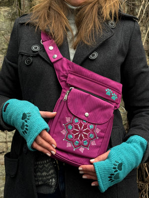 Nahaufnahme Tasche: Ein Model präsentiert die Gassi-Tasche, Hüfttasche, Bauchtasche Hannover Mandala 311 aus wasserabweisendem Stoff, Pink. Sie trägt sie als Crossbodybag über der Schulter. An den Händen trägt sie Handstulpen HADAR 48 aus Schurwolle in Türkis mit zwei Pfotenstickerei.