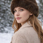 Model trägt braune Kunstfell-Wintermütze im winterlichen Outdoor-Stil
