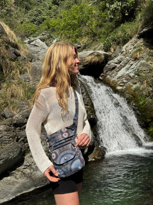 Frau steht vor einem Wasserfall mit der Gassitasche SUPER HANNOVER im Mandala-Design – perfekt für Outdoor-Abenteuer mit Hund.