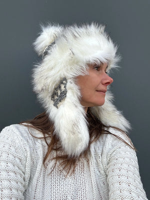 Frau trägt handgestrickte Wintermütze aus 100% Schurwolle mit Kunstfellbesatz und Bommel in Creme- und Grautönen
