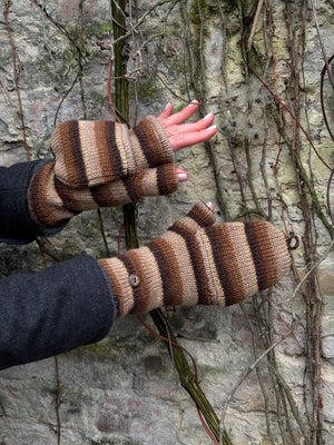 Nahaufnahme Hände: Model präsentiert fingerfreie Handschuhe aus Wolle gestreift in Brauntöne, welche sich mit einer Fingerkappe zu Fäustlingen umwandeln lassen. Zwei Tragemöglichkeiten.