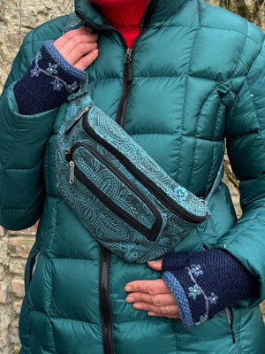 Model präsentiert Handstulpen mit Daumen aus Schurwolle in Dunkelblau und Hellblau, bestickt mit Blumengirlande. Jede Blume besitzt mittig ein Strasssteinchen. Um die Schulter trägt sie eine Crossbodybag Torino aus Baumwoll-Canvas, marineblau bedruckt mit hellblauen, floralen Ornamenten.