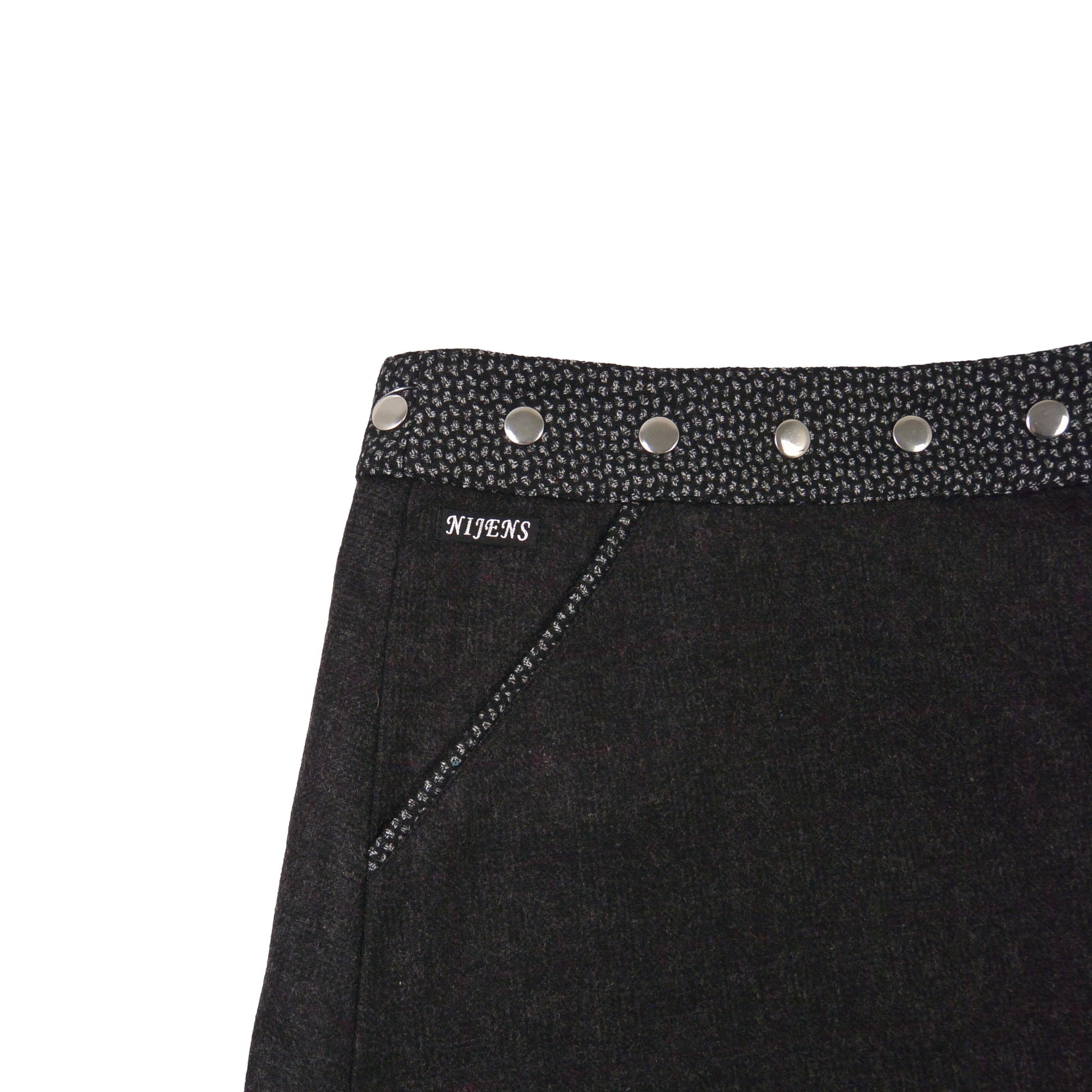 Detailaufnahme des schwarzen Tweed-Wenderocks mit silbernen Druckknöpfen und Tasche von Nijens