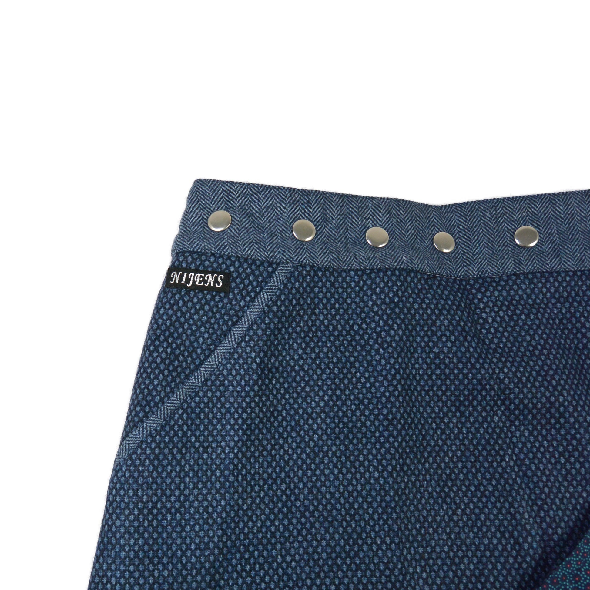 Detailaufnahme des dunkelblauen Tweed-Wenderocks mit silbernen Druckknöpfen und Tasche von Nijens