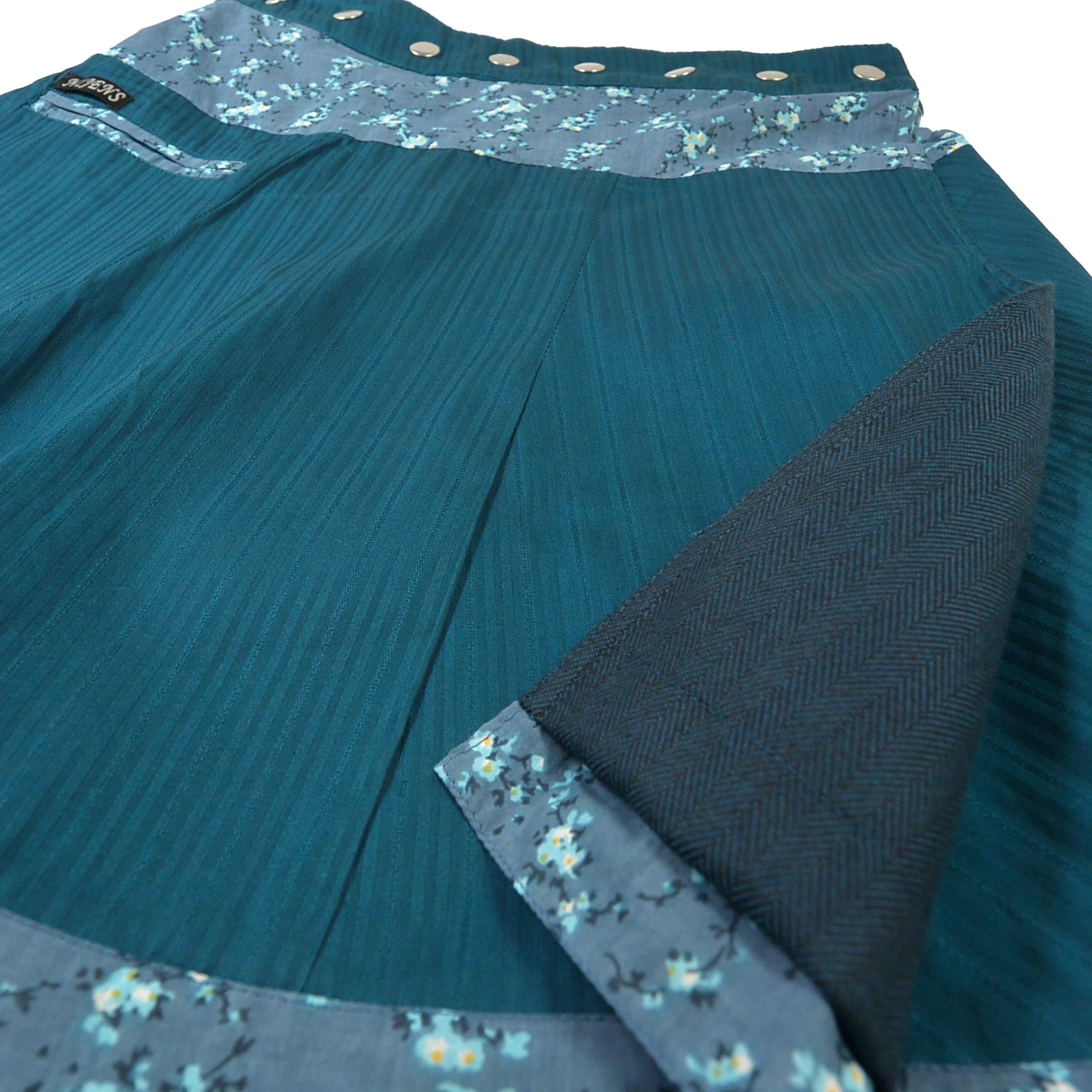 Detailaufnahme des Nijens Wenderocks in Türkis mit feiner Struktur und aufgeklappter dunkelblauer Innenseite. Reversibler Winterrock.