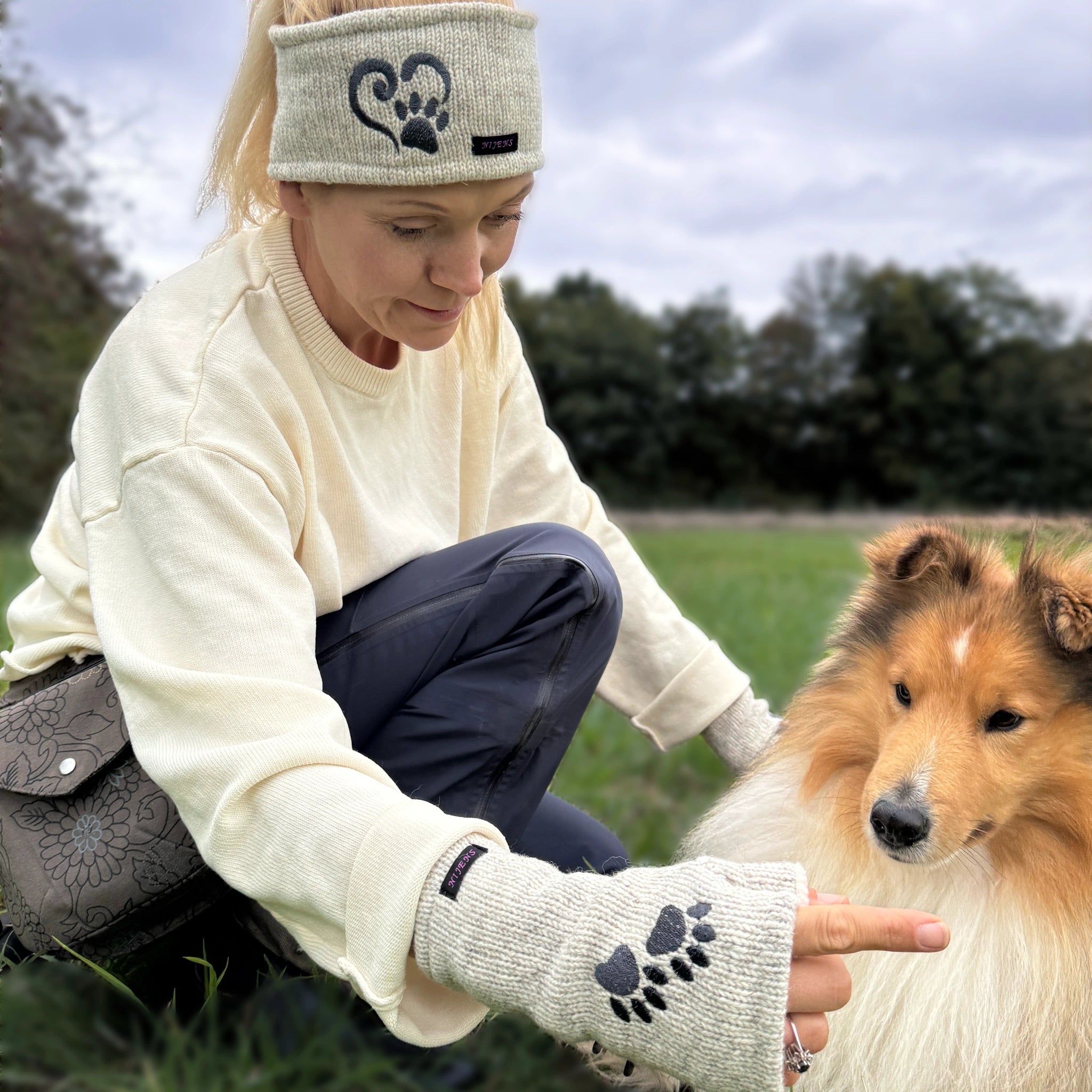 Frau beim Training mit Hund, trägt helles Woll-Stirnband und Pulswärmer mit Pfotenmotiv von Nijens