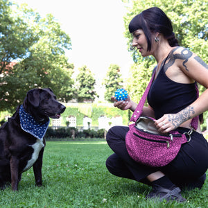 Model mit Hund im Park präsentiert Bauchtasche sowie Crossbodybag aus Canvas in Magenta, mit rosafarbenen kleinen Pfötchen in der Tragevariante über der Schulter: Crossbodybag.