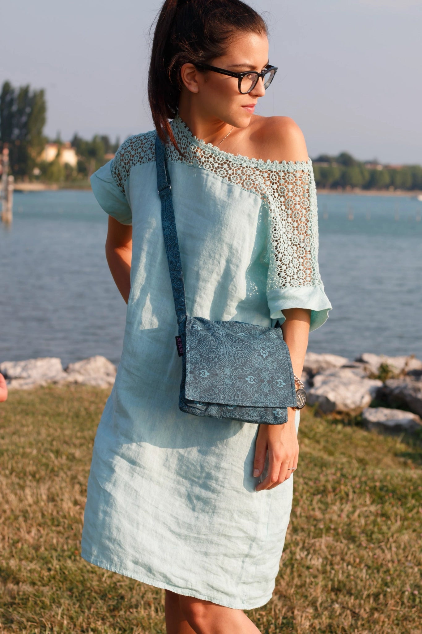 Eine Frau präsentiert kleine Tasche, Umhängetasche aus Baumwolle, Petrol mit floralen Ornamenten.