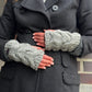 Nahaufnahme Hände: Model präsentiert handgestrickte Handstulpen, Pulswärmer aus Schurwolle grau, mit Daumenspalte und großem Zopfstrickmuster. 2