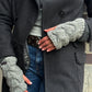 Nahaufnahme Hände: Model präsentiert handgestrickte Handstulpen, Pulswärmer aus Schurwolle grau, mit Daumenspalte und großem Zopfstrickmuster.