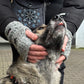 Nahaufnahme von Model, welches sich über einen Hund beugt und seinen Kopf streichelt. Um die Hüfte trägt sie eine Bauchtasche mit Mandalastickerei und an den Händen Handstulpen aus Schurwolle grau mit zwei Pfotenstickerei.
