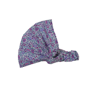 Nijens Stoff-Haarband in Lavendel mit kleinem Blumenmuster in Türkis, Rostorange und Weiß, seitlich liegend vor weißem Hintergrund