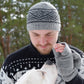 Mann trägt graue Strickmütze aus Schurwolle mit schwarzem Muster und passende Pulswärmer beim Spaziergang mit seinem Hund im Wald.