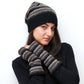 Model trägt Nijens fingerlose Pulswärmer aus Schurwolle mit Baumwollfutter in Schwarz, Grau und Braun, gestreiftes Strickdesign mit Daumenöffnung.