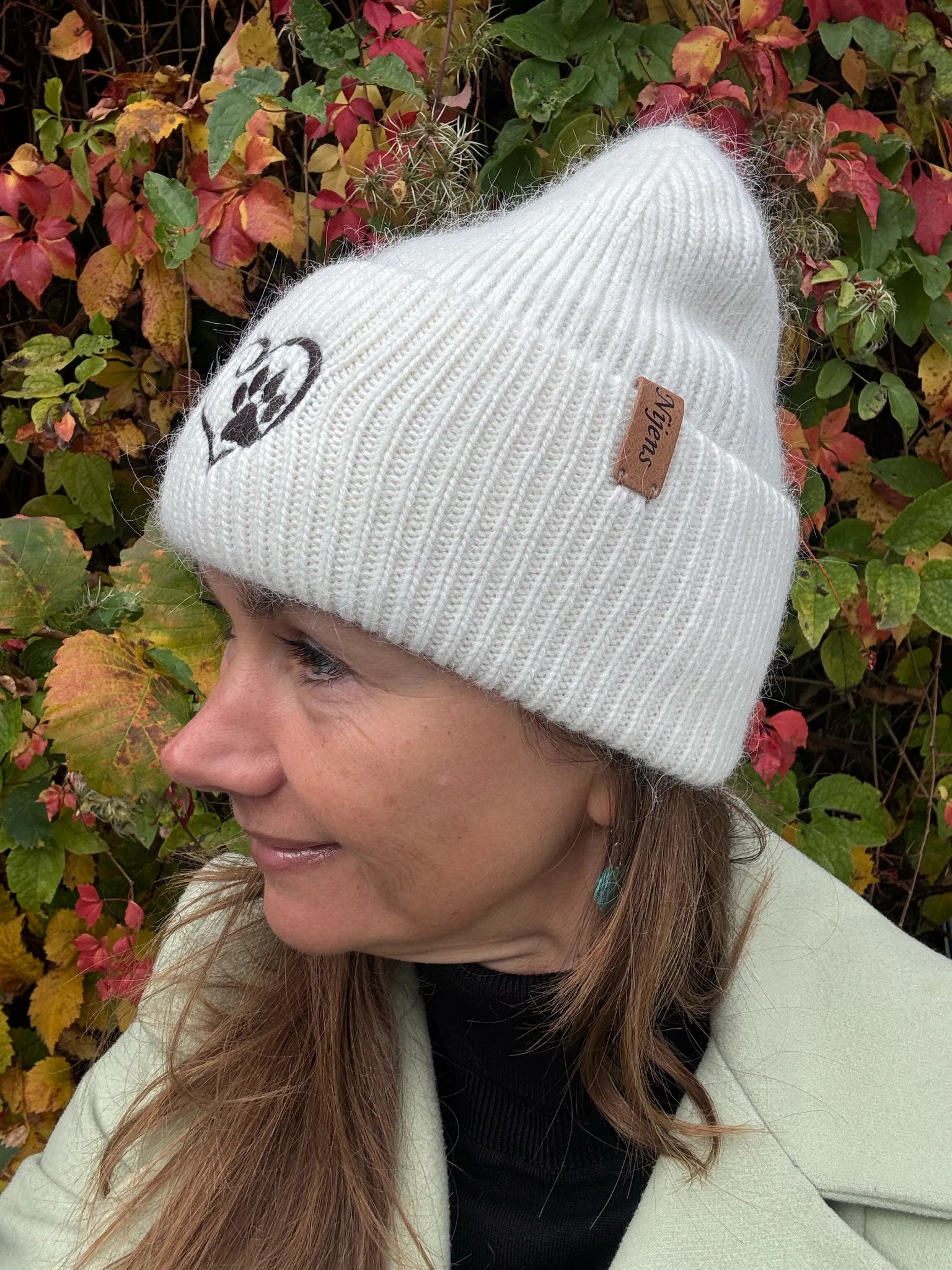 Frau trägt weiße Nijens Angora Beanie Marseille mit Pfote-&-Herz-Stickerei beim herbstlichen Spaziergang