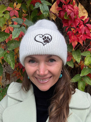 Nahaufnahme einer Frau mit weißer Nijens Angora Beanie Marseille und Pfote-&-Herz-Stickerei vor bunten Herbstblättern