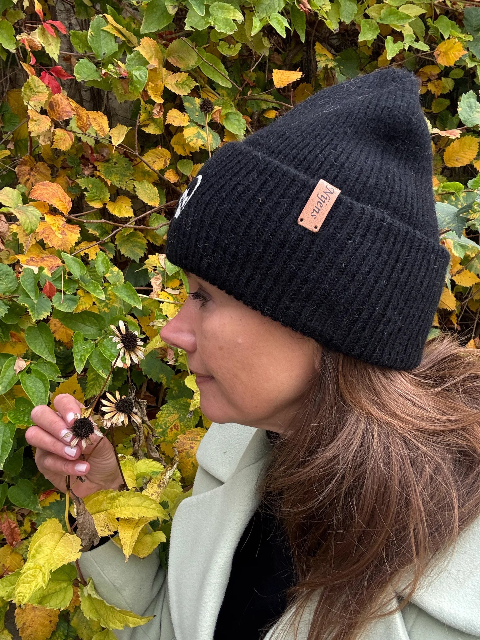 Frau trägt schwarze Nijens Angora Beanie Marseille mit Pfote-&-Herz-Stickerei beim herbstlichen Spaziergang