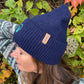 Seitliche Ansicht einer Frau mit dunkelblauer Nijens Angora Beanie Marseille und Pfote-&-Herz-Stickerei vor herbstlichem Hintergrund